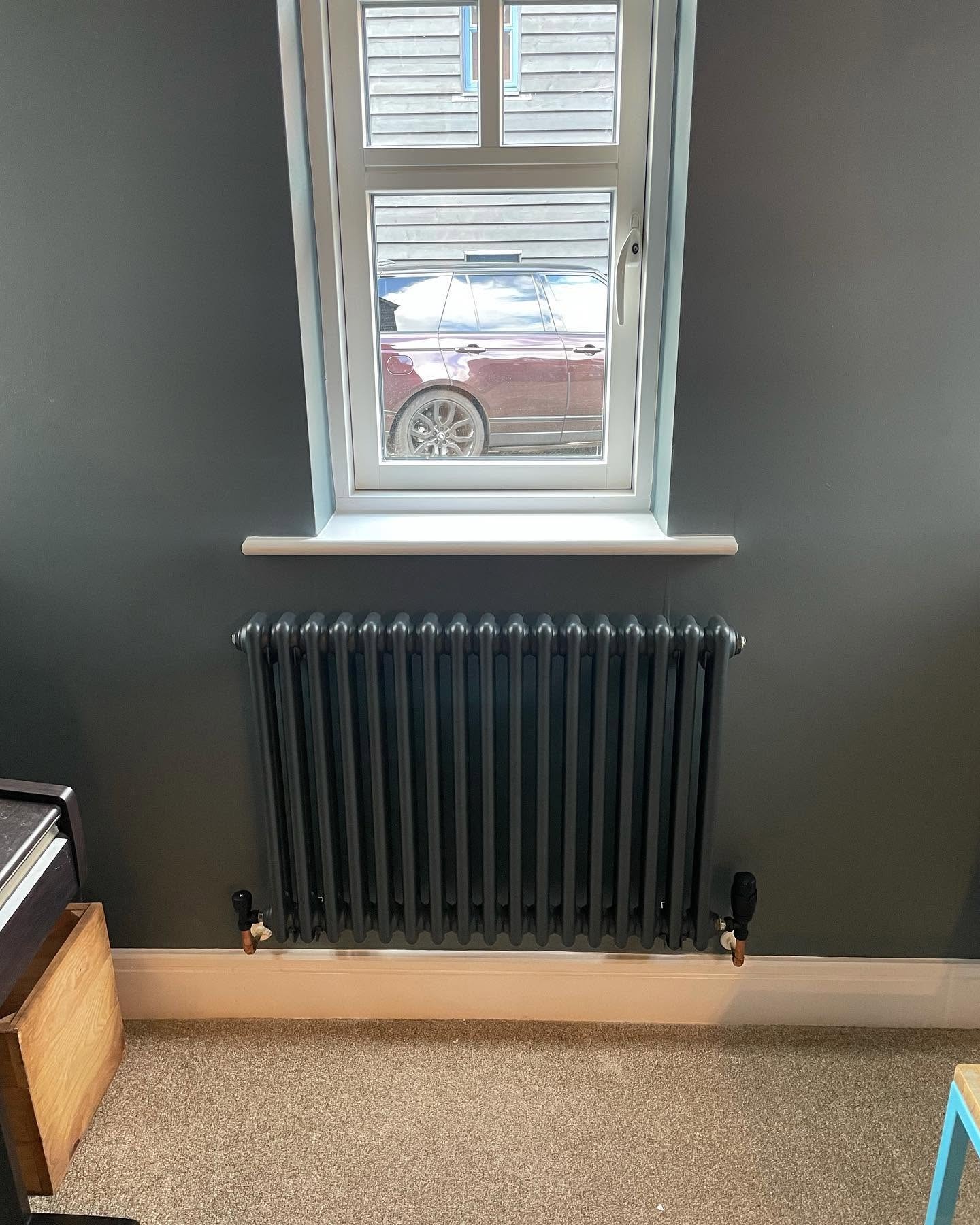 Dark grey column radiator installed under a window during a heating upgrade